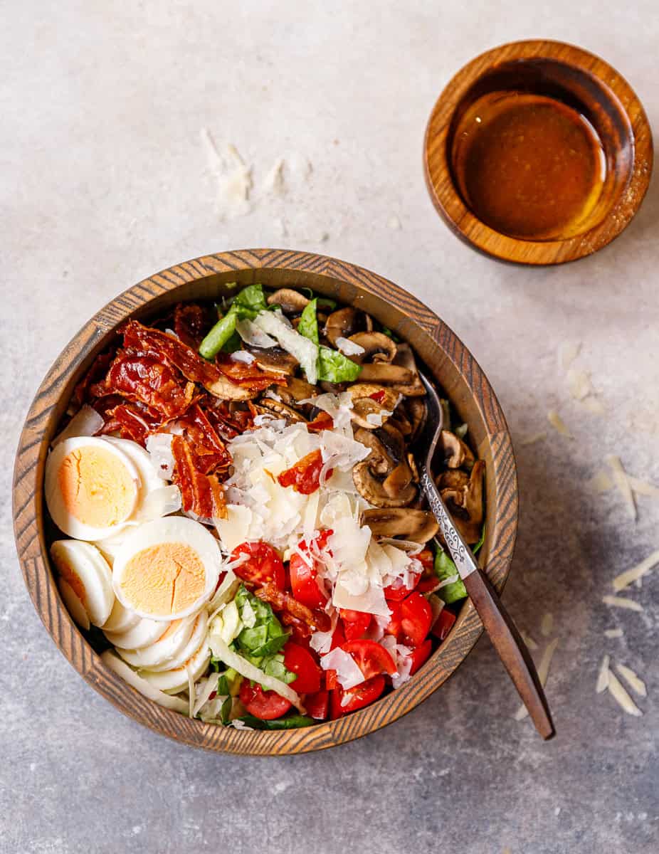 Top-down shot of deconstructed mushroom salad with dressing on the side and ingredients grouped in a wooden bowl.