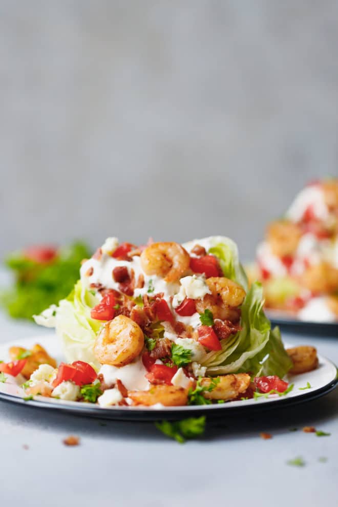 Iceberg lettuce wedge salad with shrimp, bacon and blue cheese dressing on an enamelware plate