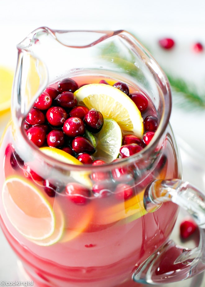 Cranberry Orange Punch in a clear festive pitcher, topped with fresh cranberries, lime and lemon slices
