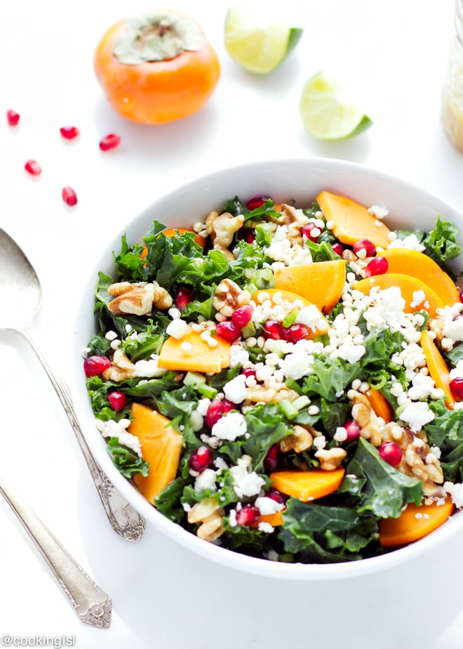 A bowl full with kale persimmon salad, topped with walnuts, millet, pomegranate and light dressing.