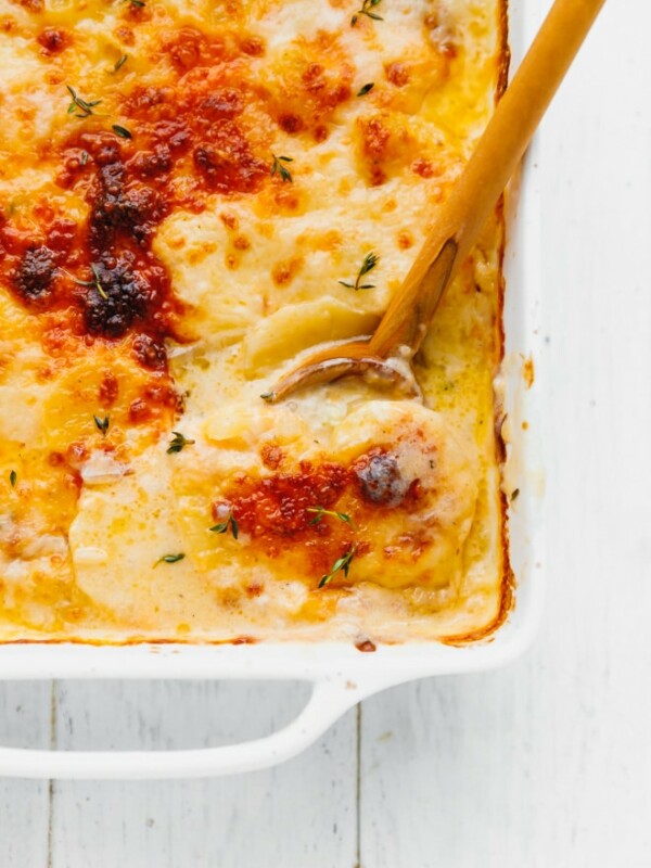 Scalloped potatoes with cheddar in a baking dish with wooden spoon