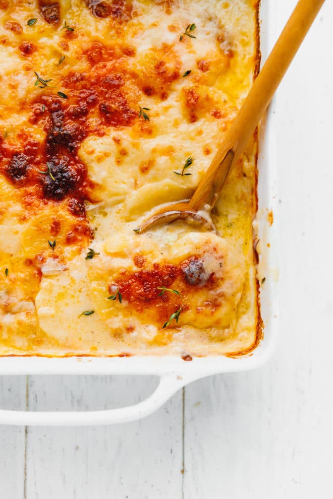 Scalloped potatoes with cheddar in a baking dish with wooden spoon