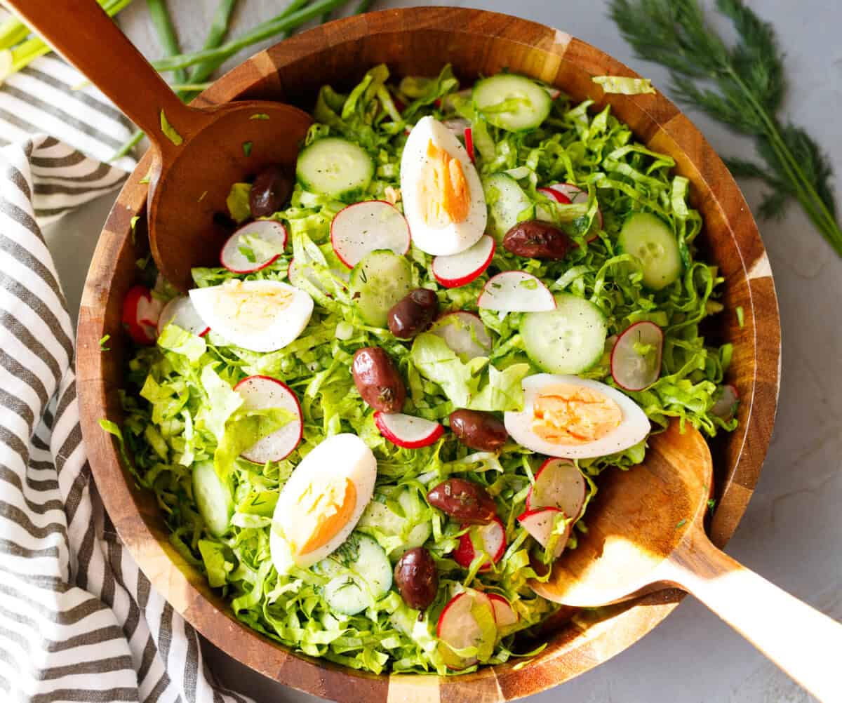 Bulgarian green salad with lettuce, cucumbers, radishes, eggs and olives served in a wooden bowl