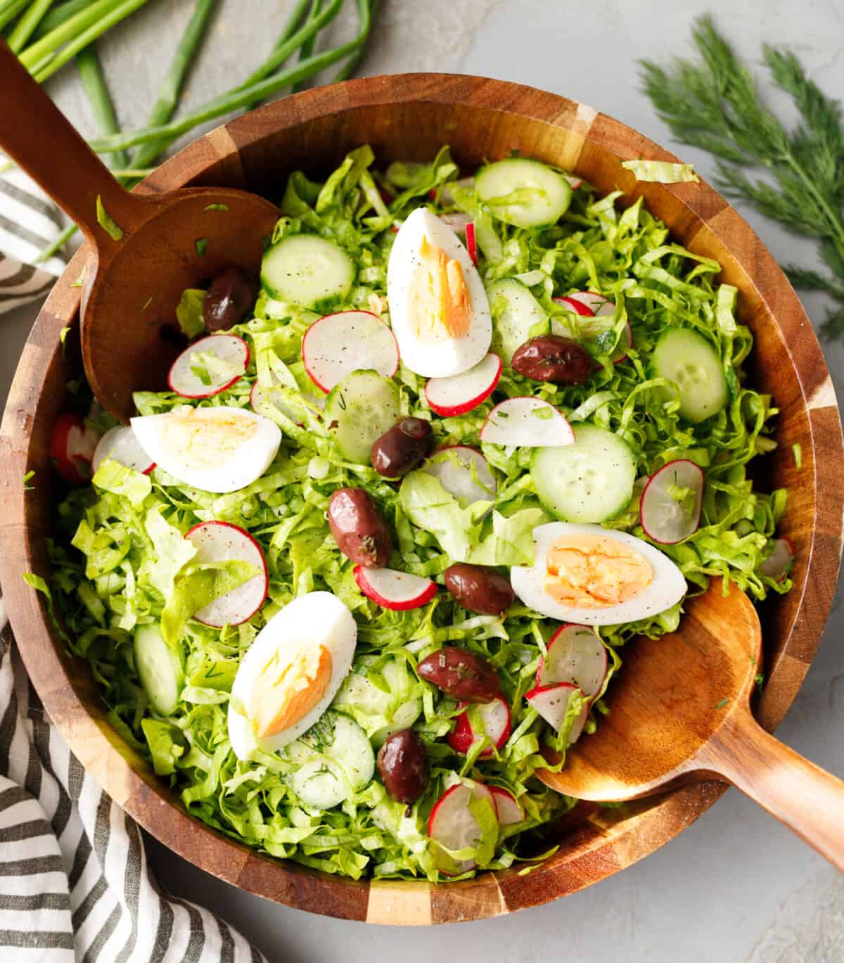Bulgarian green salad with lettuce, cucumbers, radishes, eggs and olives served in a wooden bowl