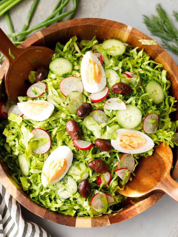 Bulgarian green salad with lettuce, cucumbers, radishes, eggs and olives served in a wooden bowl