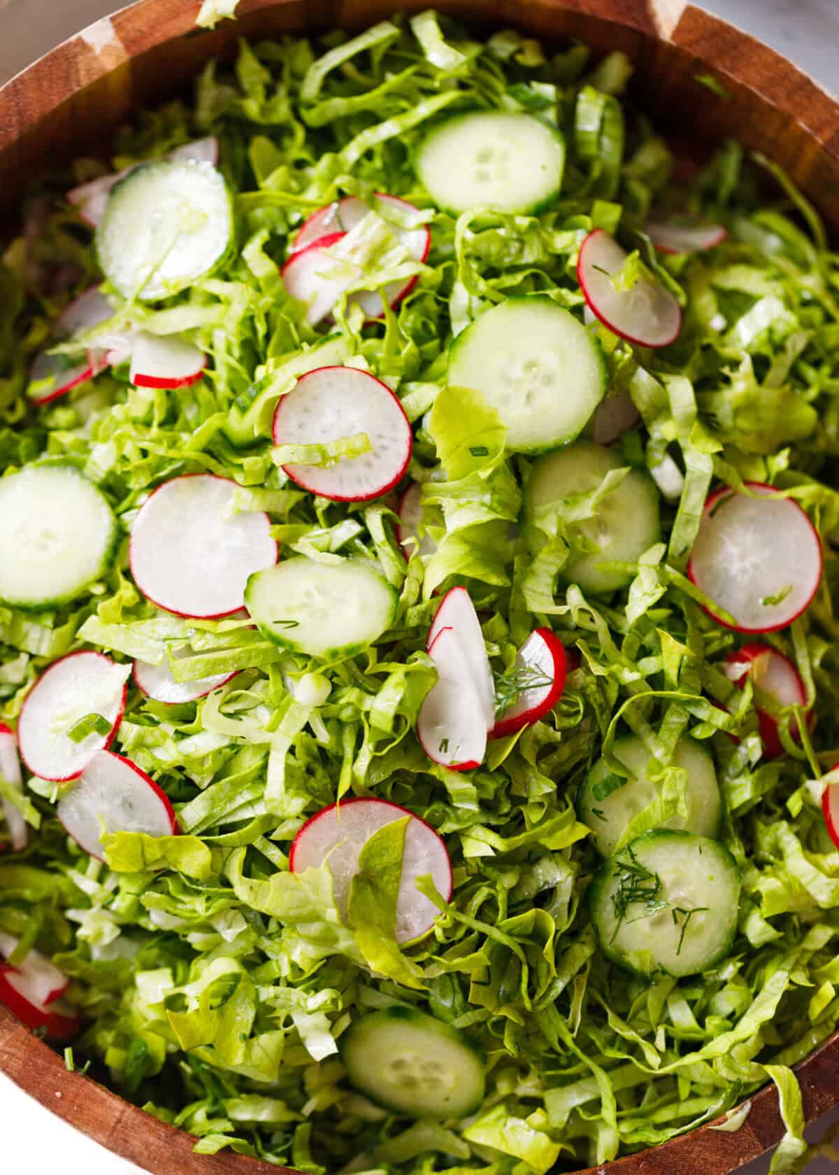 Bulgarian green salad with lettuce, cucumbers and radishes in a wooden bowl