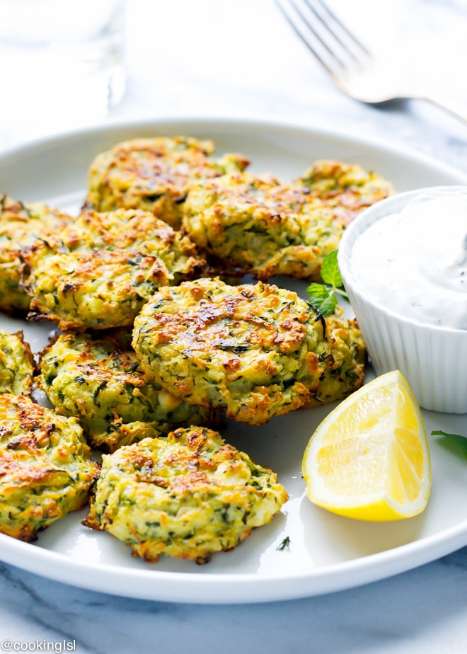 zucchini and feta fritters on a plate with lemon wedge
