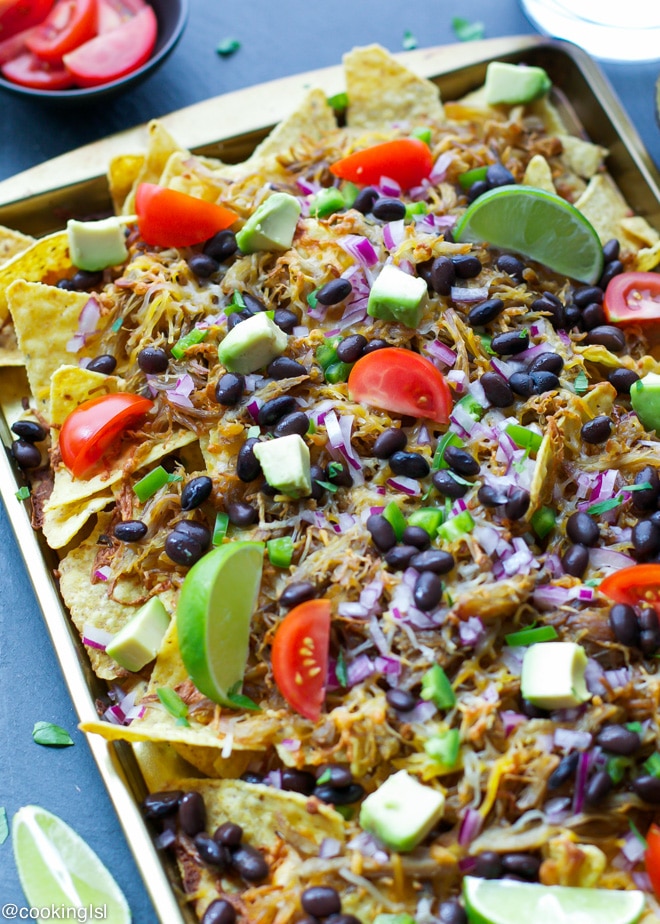 Pulled pork Nachos Recipe, on a heatproof pan, topped with fresh tomatoes, lime and avocado.