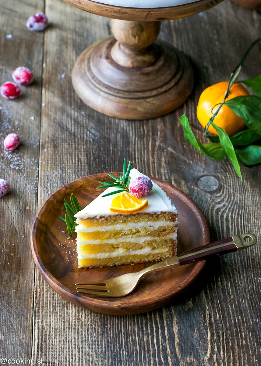 Tangerine Layer Cake With Tangerine Curd And Cream Cheese Frosting Recipe. On a wooden cake pedestal, with a slice of cake on the side on a wooden plate.