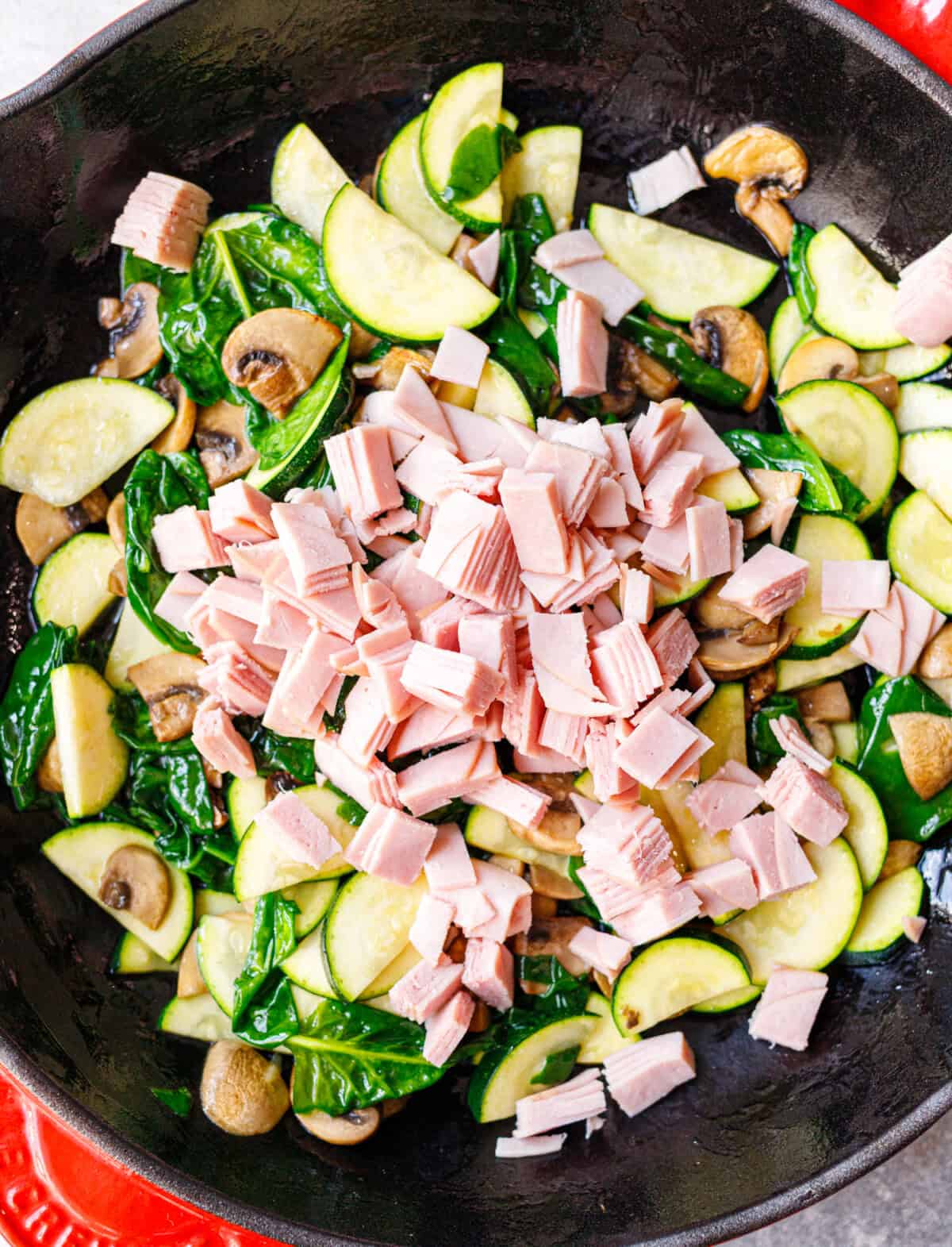 Chopped ham added on top of sautéed zucchini, mushrooms, and spinach in a cast iron skillet