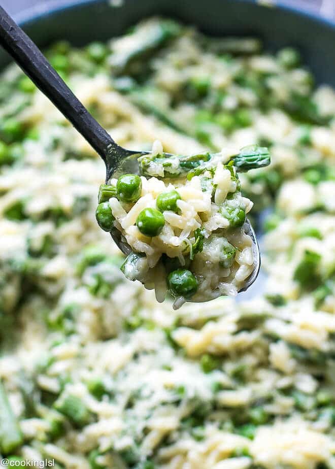 A spoon full of creamy orzo pasta. Orzo with fresh asparagus, peas and parmesan. One pot/skillet pasta.