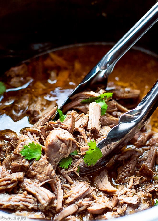 Juicy tender easy slow-cooker Barbacoa recipe. Beef with sauce in a crock pot, topped with cilantro.