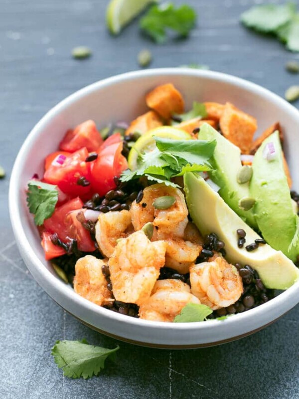 Grain bowl with black rice, black qionoa, black lentils, sliced avocado, shrimp, roasted sweet potoato cubes, tomatoes and topped with cilantro and pumpkin seeds.
