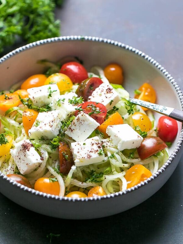 A bowl full with spiralized cucumber, chopped cherry tomatoes, onion, parsley, olive oil, salt, apple cider vinegar and cubed feta cheese, sprinkled with sumac.