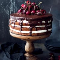 A wooden cake stand with gorgeous cherry, whipped cream, chocolate cake. Easy black forrest cake recipe, perfect for a summer celebration.