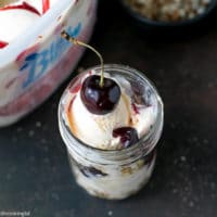 Cherry Sundae Recipe - step by step photos. Mason Jar with crushed cookies, Blue Bunny® Cherrific Cheesecake Ice cream, fresh cherries, coconut and chopped almonds. Topped with a fresh cherry on top.