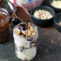 Cherry Sundae Recipe - step by step photos. Mason Jar with crushed cookies, Blue Bunny® Cherrific Cheesecake Ice cream, fresh cherries, coconut and chopped almonds. Topped with a fresh cherry on top and drizzled with chocolate sauce.