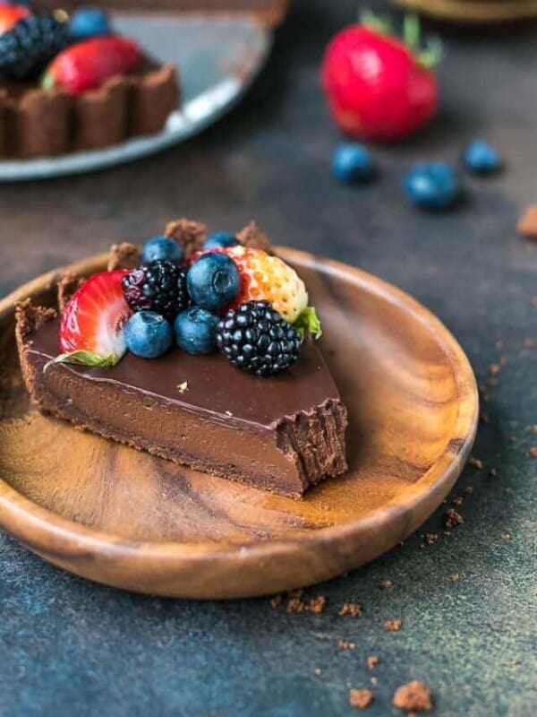 A wooden bamboo plate with a slice of decadent and delicious dark chocolate tart, topped with fresh berries.