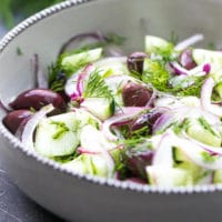 A bowl with Cucumber And Onion Salad With Apple Cider Vinegar And Olives, Tender english cucumber, red onion and kalamata olives.