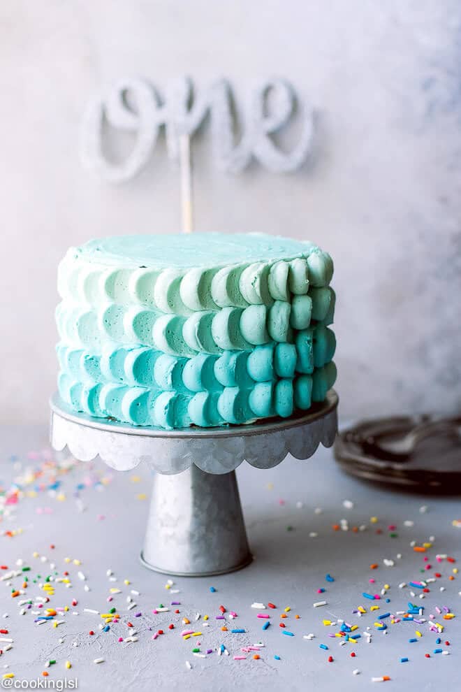 One year old, baby's first birthday glitter cake topper. Ombre blue cake, decorated with buttercream petals. Homemade funfetti birthday cake.