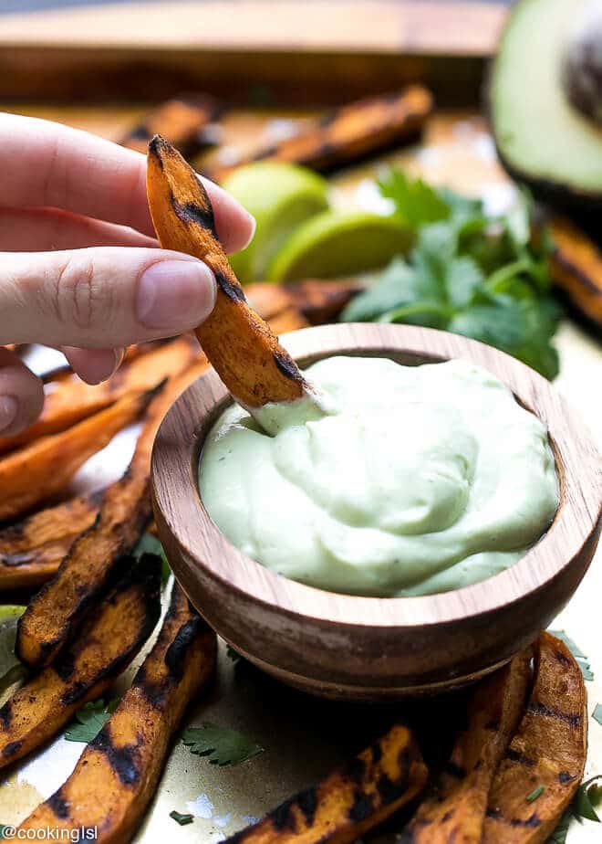 How To Grill Sweet Potato Fries-a small acacia wooden dip bowl fille with avocado yogurt dipping sauce and grilled sweet potato fries dipped in it.