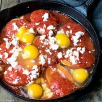A plate with Potatoes With Tomato Sauce Feta And Eggs , runny egg yolk and delicious tomato sauce and potatoes combination. Eggs with potatoes and feta in a cast iron skillet.