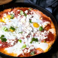 A plate with Potatoes With Tomato Sauce Feta And Eggs , runny egg yolk and delicious tomato sauce and potatoes combination. Eggs with potatoes and feta in a cast iron skillet.