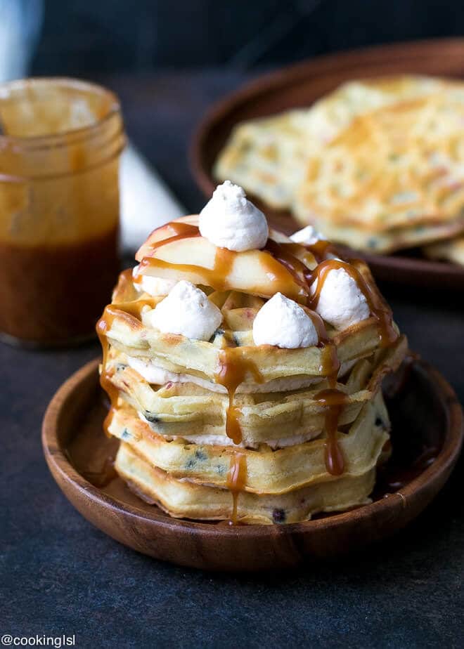 Caramel Apple Waffle Cake Recipe - waffle cake on a wooden plate with whipped cream and apples on top.