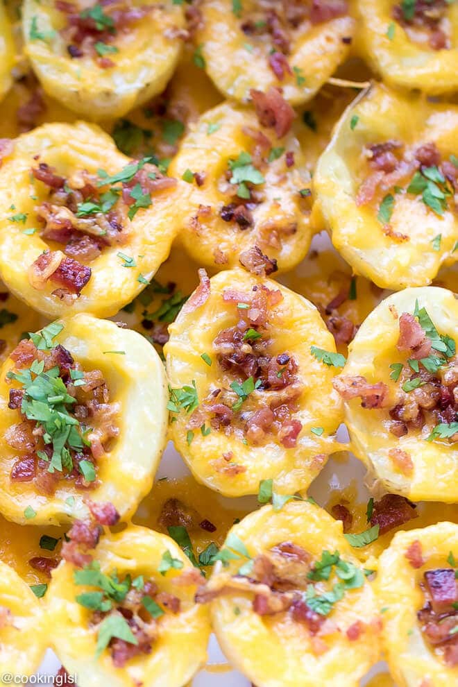 Cheesy Crispy Baked Potato Bites Recipe - boiled potatoes on a epicurean baking dish, with the inside scooped out, topped with cheese and bacon, garnished with parsley.