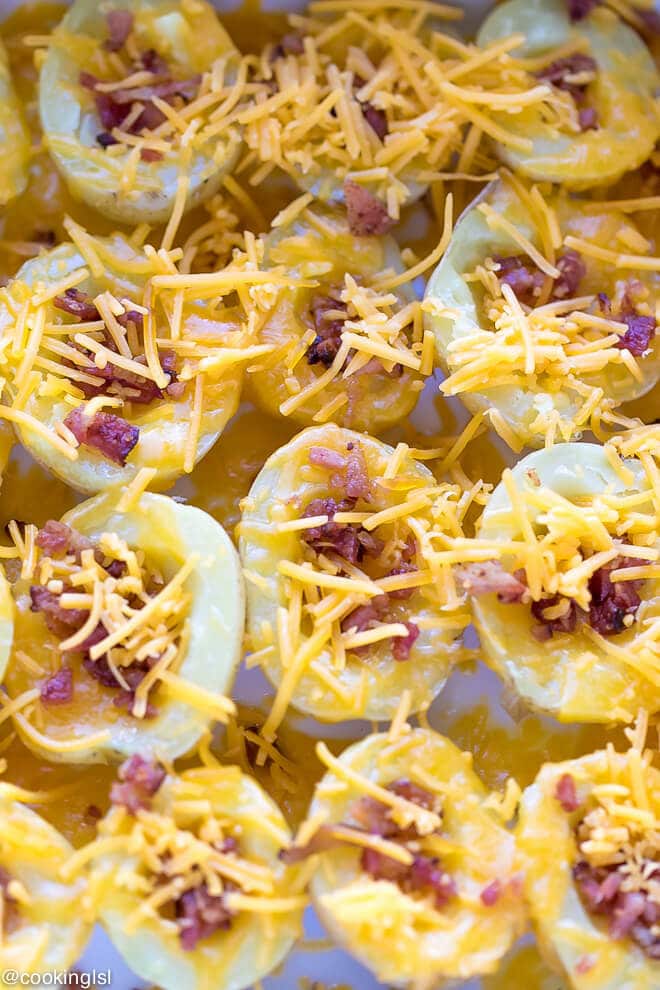 Cheesy Crispy Baked Potato Bites Recipe - boiled potatoes on a epicurean baking dish, with the inside scooped out, topped with cheese and bacon.