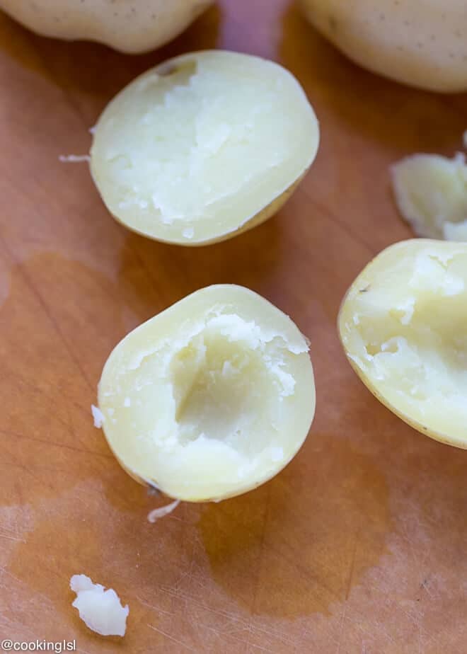 Cheesy Crispy Baked Potato Bites Recipe - boiled potatoes on a epicurean cutting board, with the inside scooped out.