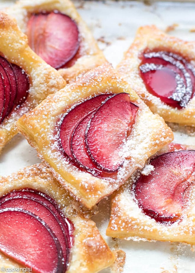 Easy Mini Plum Tarts Recipe With Puff Pastry. Square puff pastry tarts, dusted with powdered sugar, stacked on top of each other.