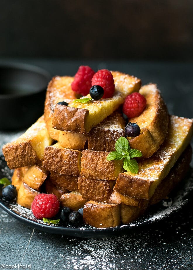 Baked French Toast Sticks Recipe on a plate, dusted with sugar and topped with berries.