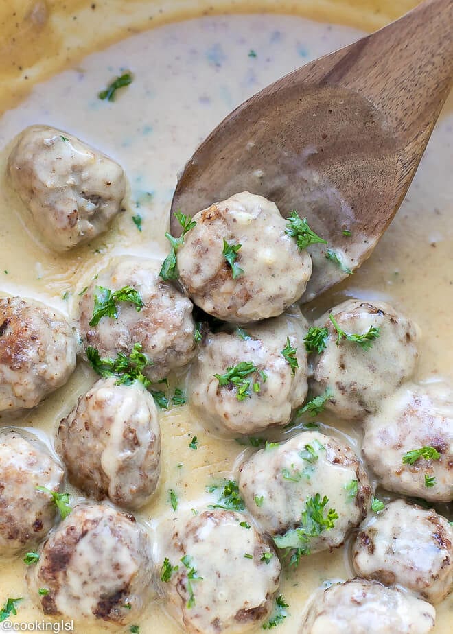 Meatloaf Meatballs With Creamy Sauce Recipe- small meatballs in a pan, topped with parsley, with a lot of sauce and wooden spoon.