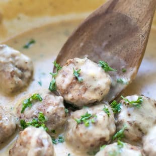 Meatloaf Meatballs With Creamy Sauce Recipe- small meatballs in a pan, topped with parsley, with a lot of sauce and wooden spoon.