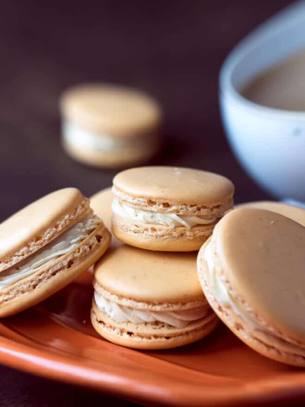 Pumpkin Spice Macarons Recipe on a fall orange plate with coffee on the side. Step by step instructions.