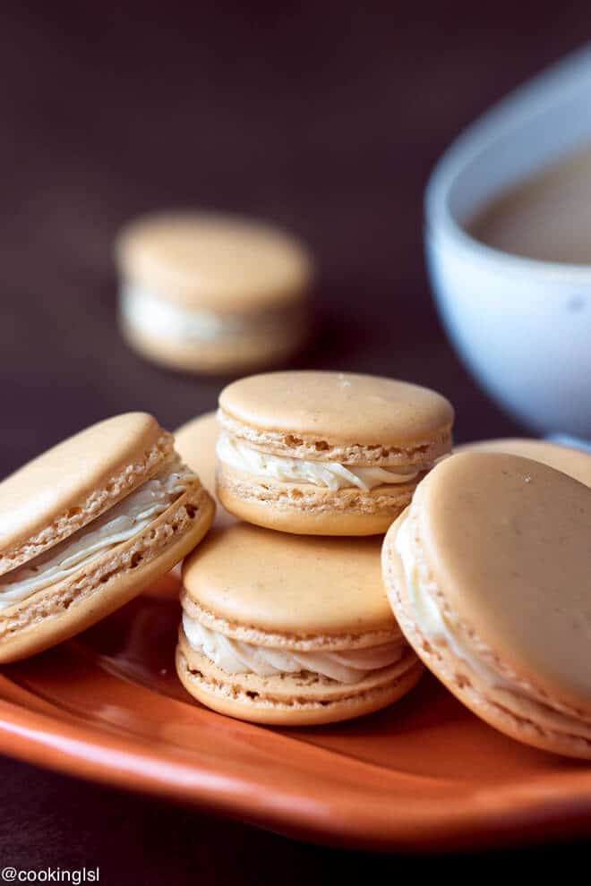 Pumpkin Spice Macarons Recipe on a fall orange plate with coffee on the side. Step by step instructions.