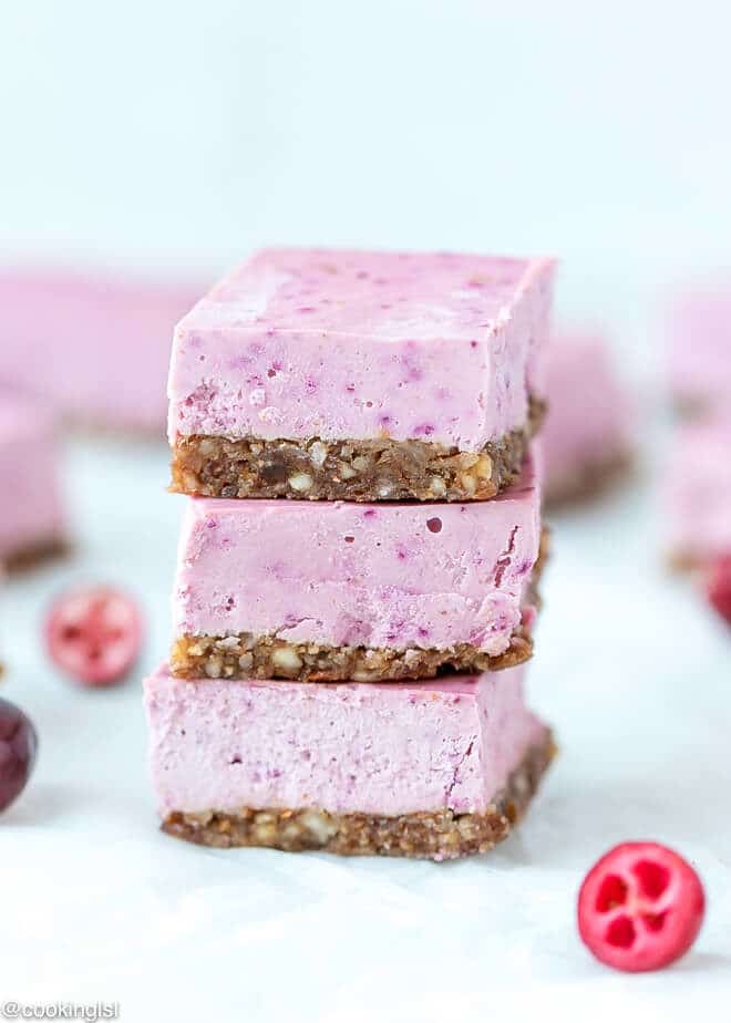 Raw Vegan Cranberry Cheesecake Bars Recipe - stacked on top of each other with cranberries on the side.