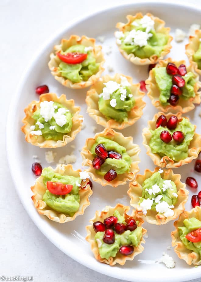 Avocado Filo Cups - Simply Avocado Sea Salt And Garlic Herb Dips, mini fill quiche shells filled with avocado dip on a platter, topped with feta, pomegranate seeds and chopped tomatoes.