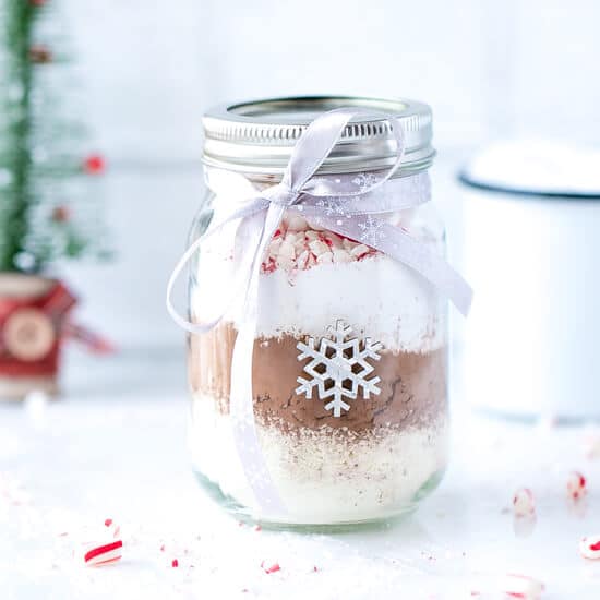 A 16 oz Ball Jar with Hot Cocoa Mix In A Jar, decorated With Christmas ribbon (bow) and stickers, Optional free printable.