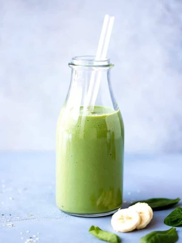 Spirulina Smoothie Recipe garnished with banana slices and baby spinach.