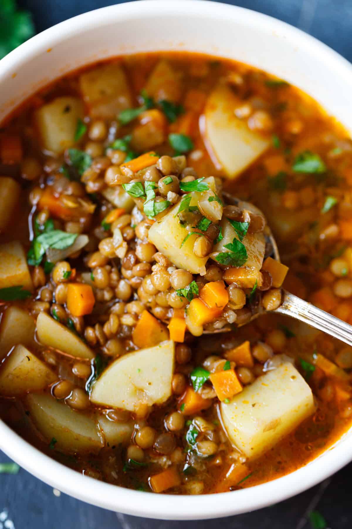 Spoon lifting lentil potato soup with chunks of potato, lentils, and carrots from a bowl