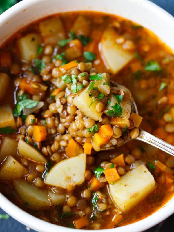 Spoon lifting lentil potato soup with chunks of potato, lentils, and carrots from a bowl