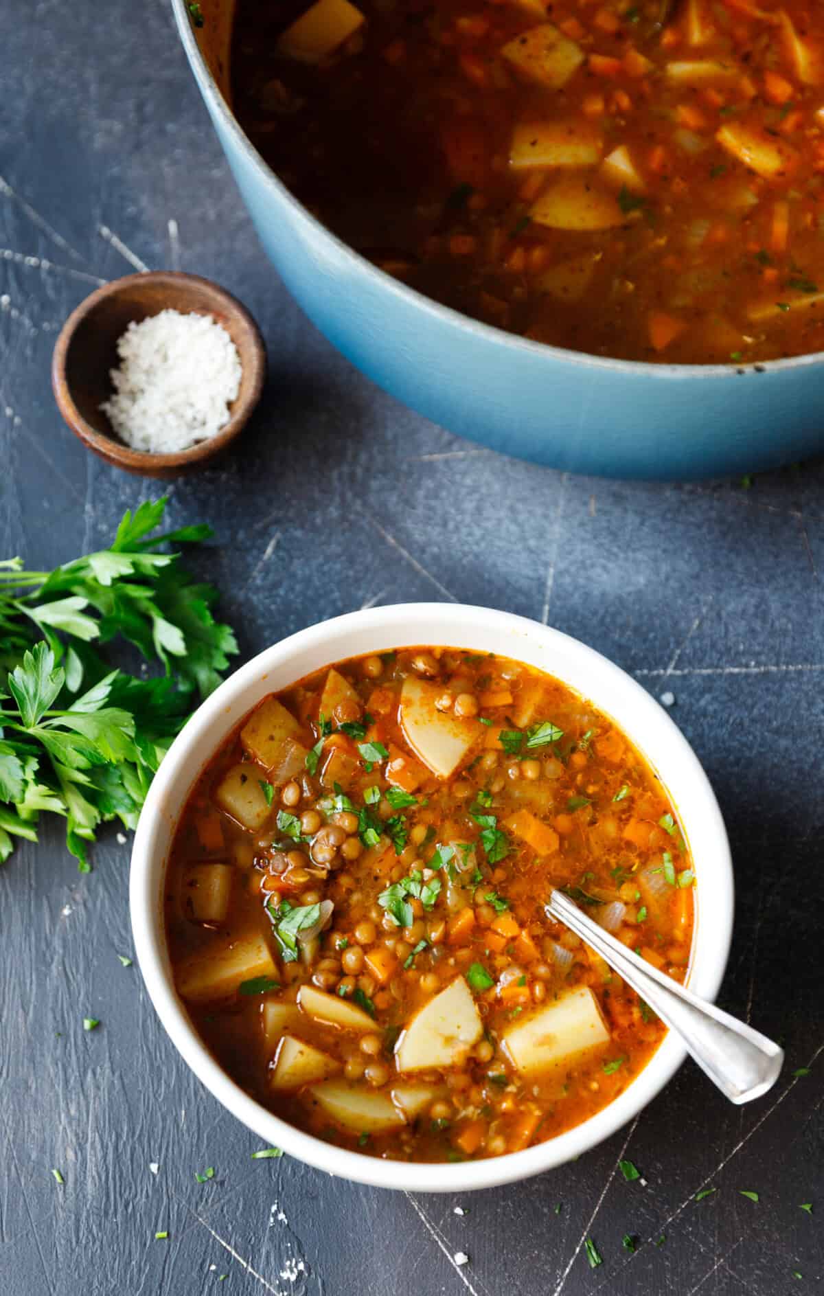 Overhead of lentil potato soup in a white bowl with parsley and a blue pot in the background