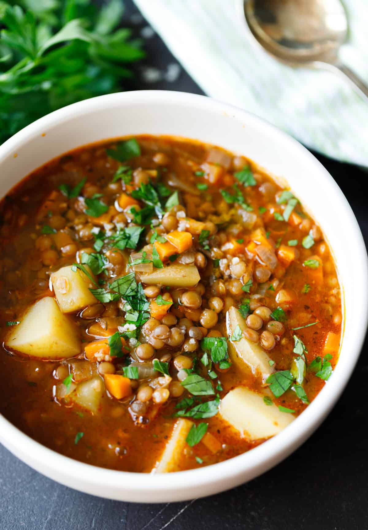 Bowl of lentil potato soup with carrots, potatoes, and fresh parsley on top