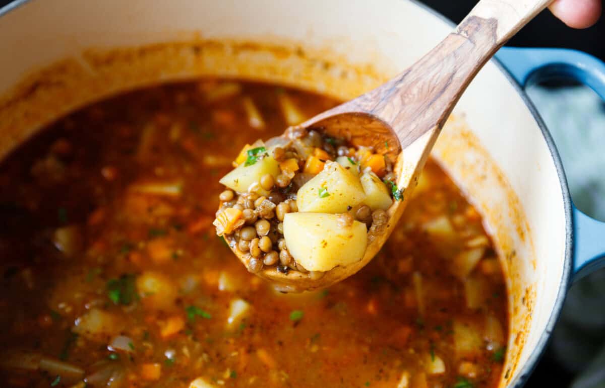 Wooden ladle lifting lentil potato soup with diced potatoes, carrots, and lentils