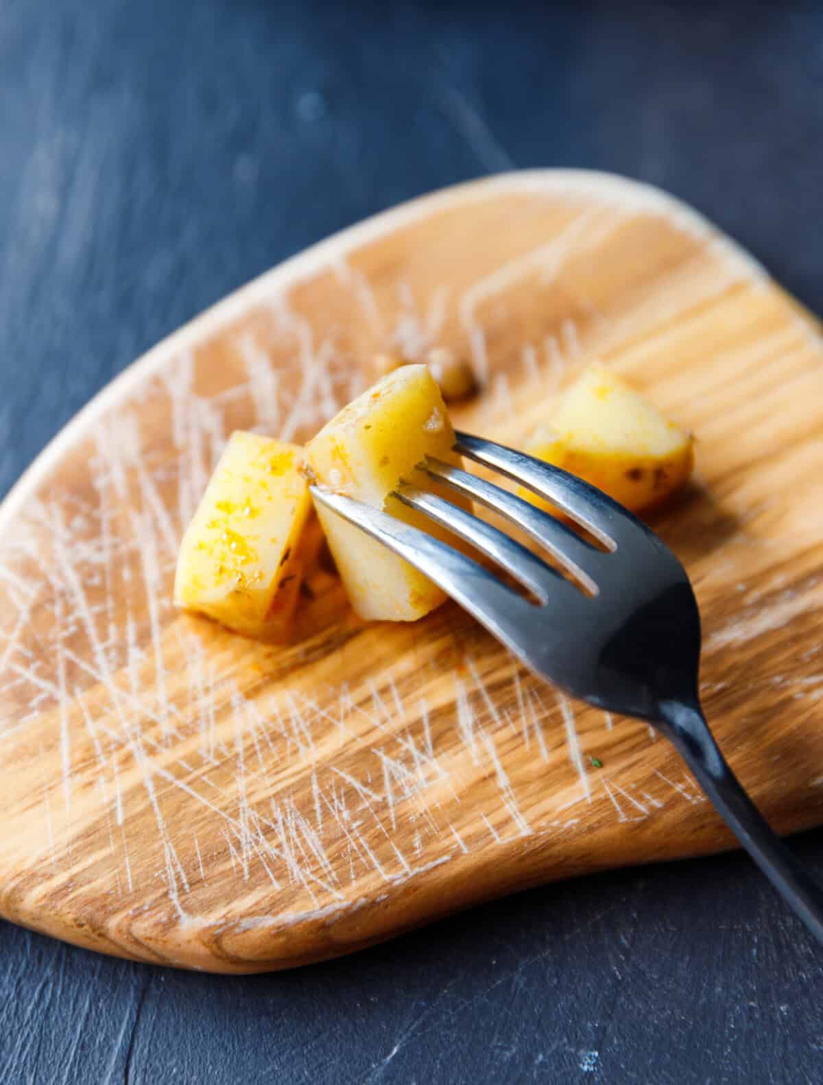 Fork piercing a cooked potato cube to check tenderness for lentil soup