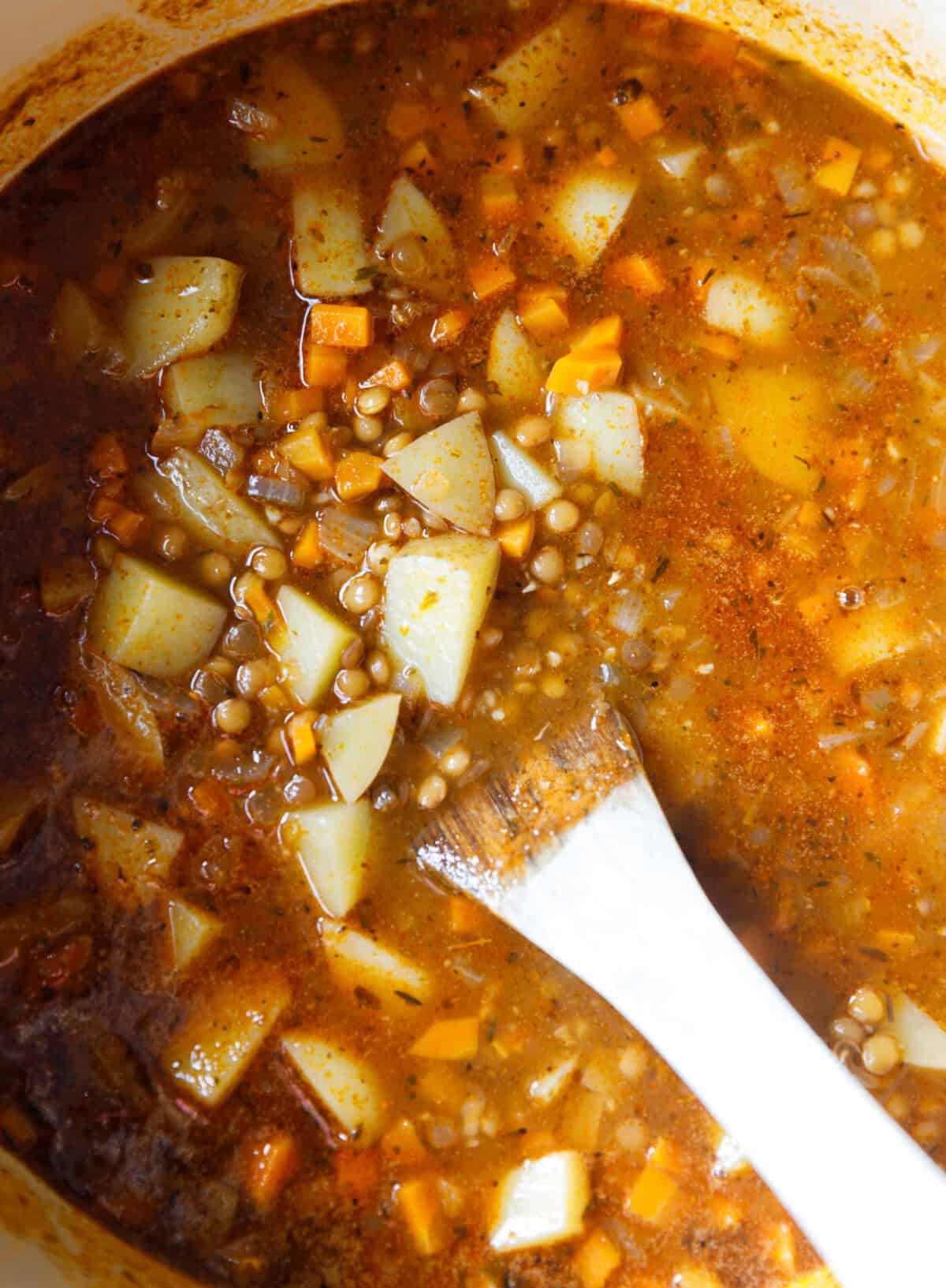 Lentil potato soup simmering in a Dutch oven with carrots, onions, and herbs