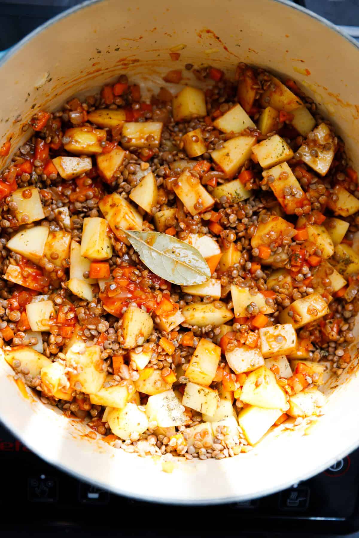 A Dutch oven with sauteed onions, carrots and garlic and tomato paste and sauce, seasonings, lentils and potatoes inside.