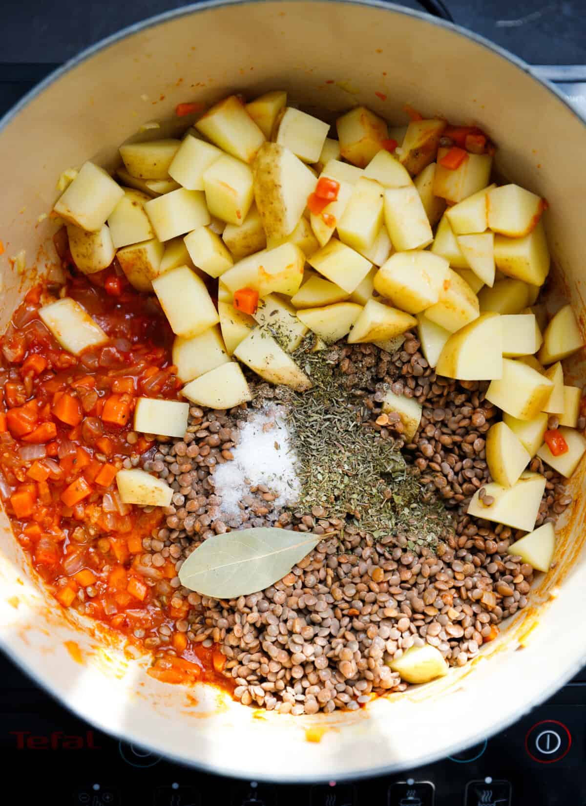 A pot with carrots, onions, garlic, seasonings, lentils and potatoes for easy lentil potato soup.